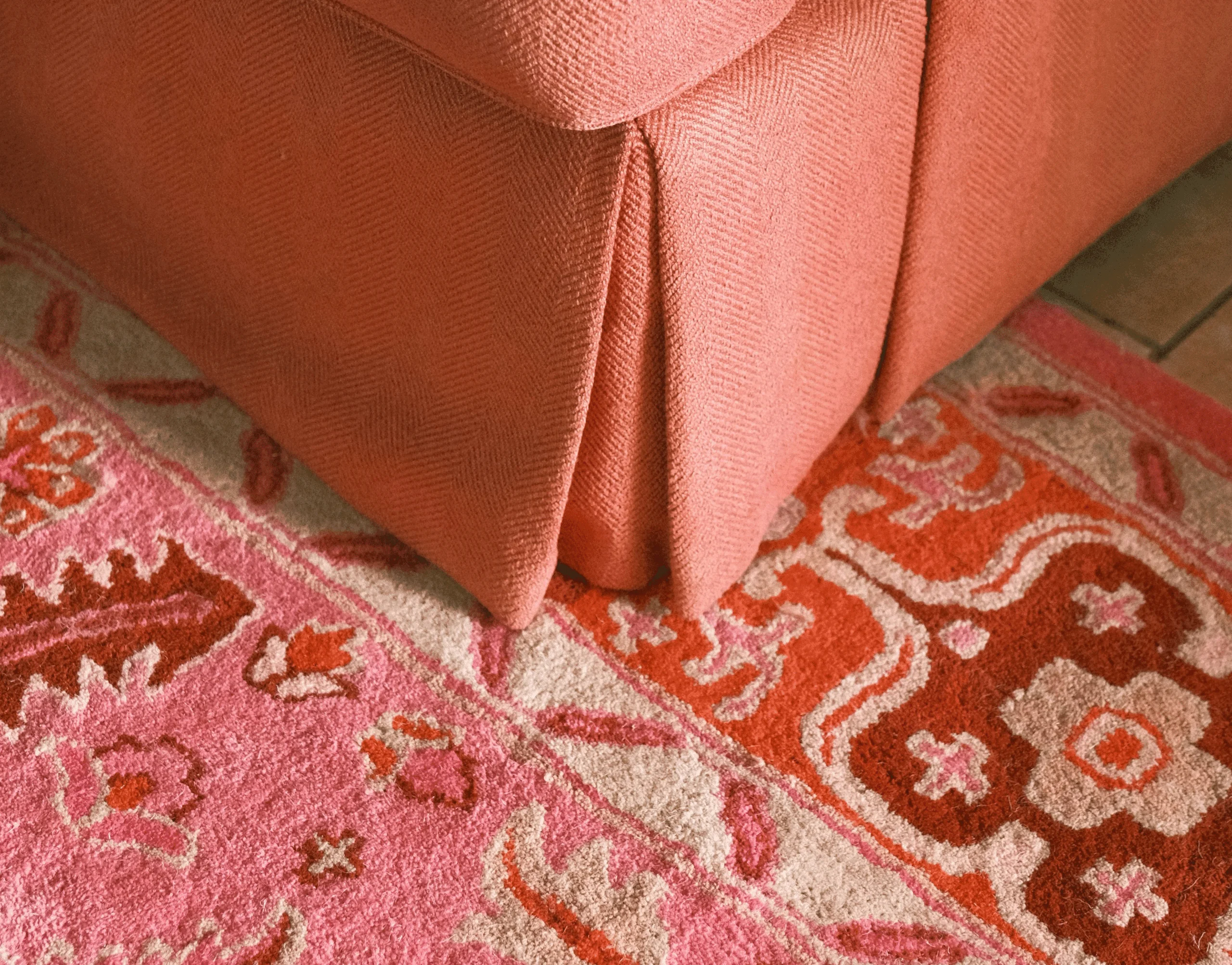 Gros plan sur un canapé en tissu texturé rose et un tapis moelleux à motifs orientaux dans les tons rose, corail et terracotta, créant une ambiance chaleureuse et enveloppante.